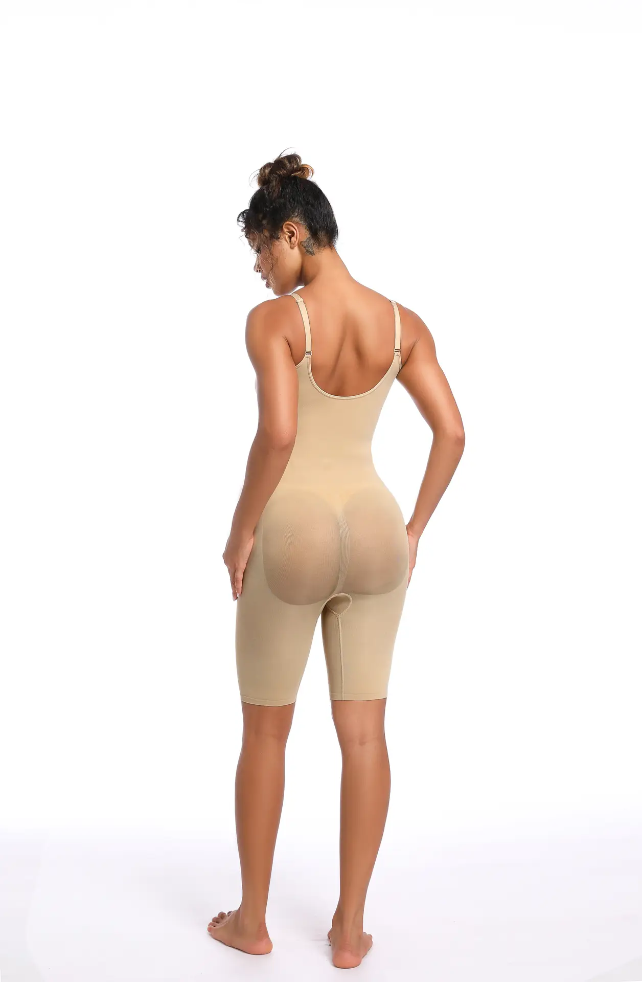 Black woman poses wearing a beige mid-thigh bodysuit facing her backside