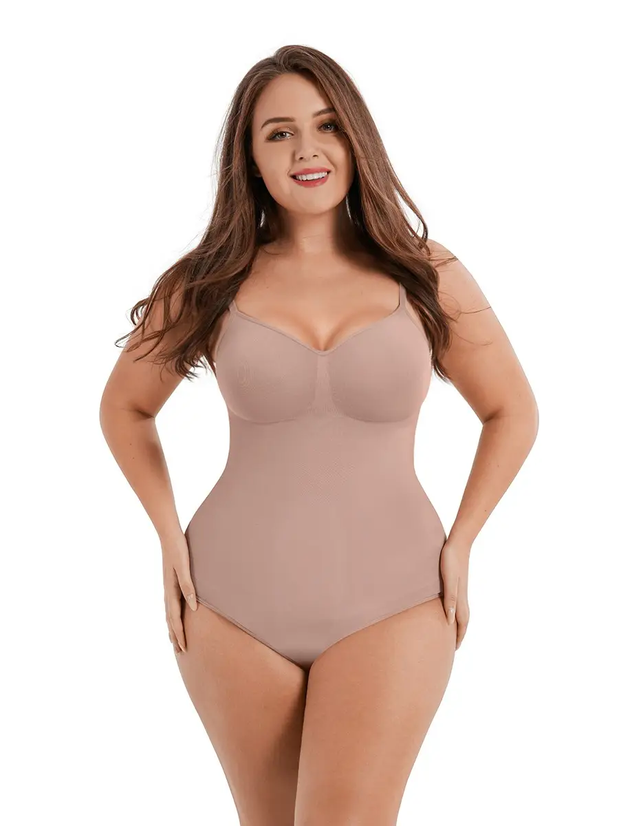 Caucasian woman posing and wearing a beige thong bodysuit over a white background