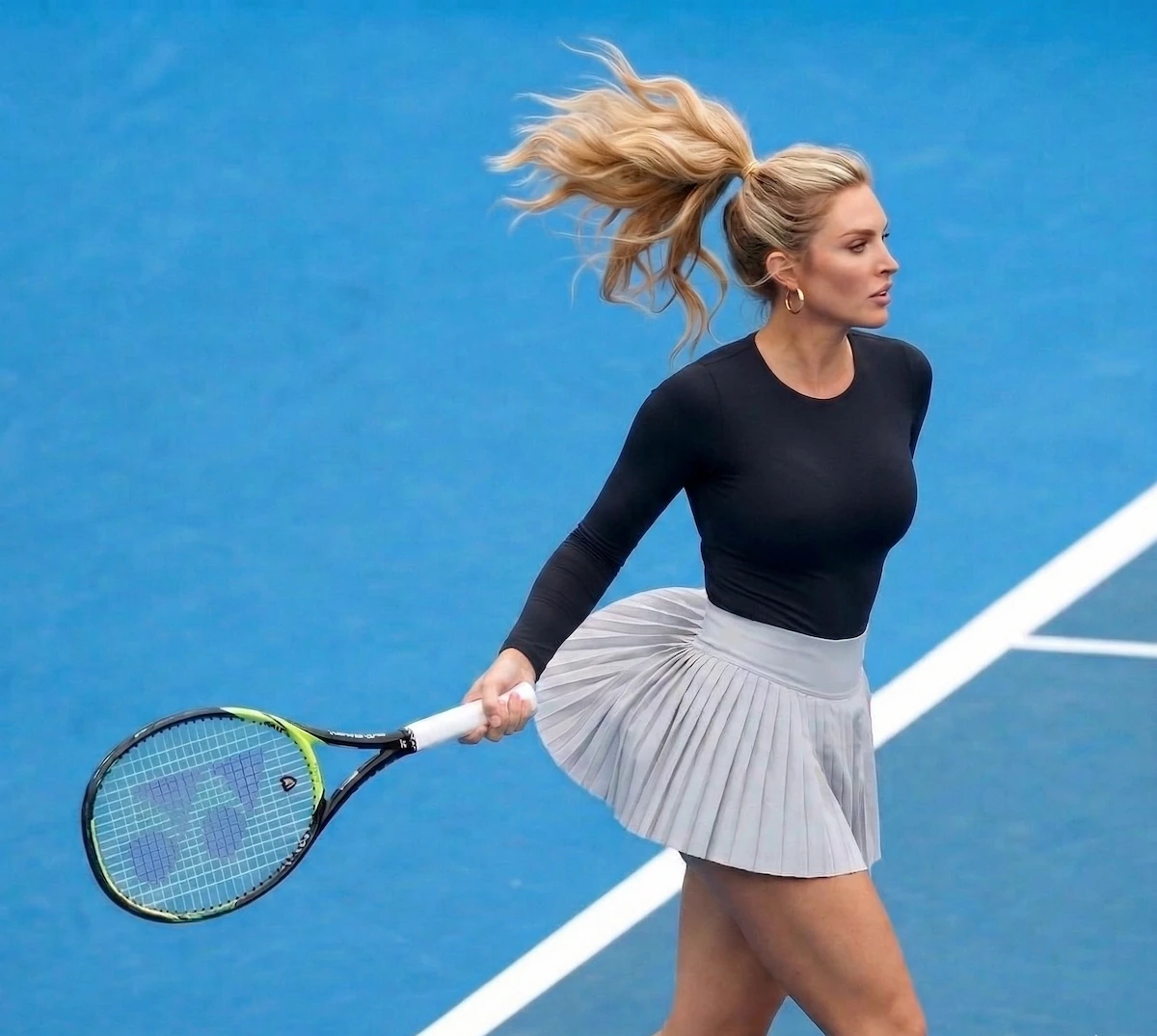 Model wearing a CALIFLO's Snatched Activewear Bodysuit While Playing Tennis Woman wearing a black long sleeve bodysuit with tennis skirt in a blue court