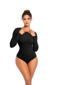 CALIFLO Casual Chic Long Sleeve Crew Neck Bodysuit black frontal 6 A women staring directly at the camera in a black, one piece, long sleeve, thong bodysuit, with large industrial door fram...